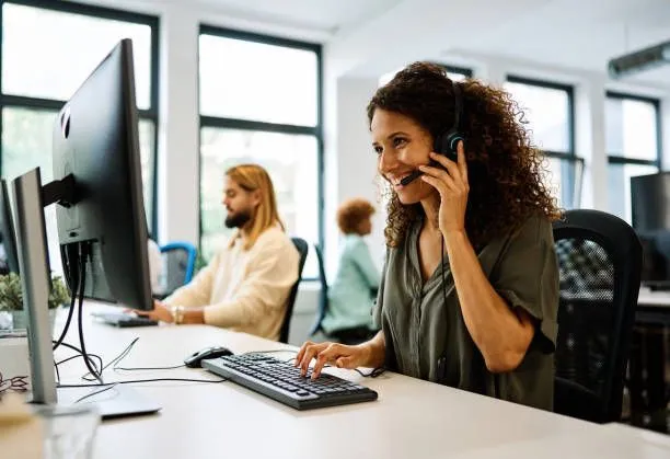A woman takes a phone call at her desk in a busy office