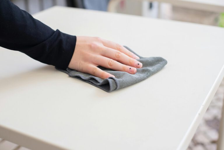 A hand wiping a white table clean with a cloth