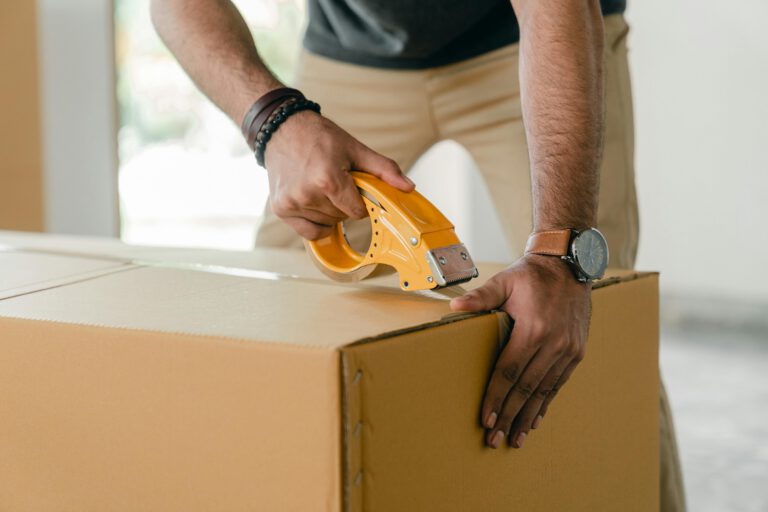 A man sealing a cardboard box with a tape dispenser