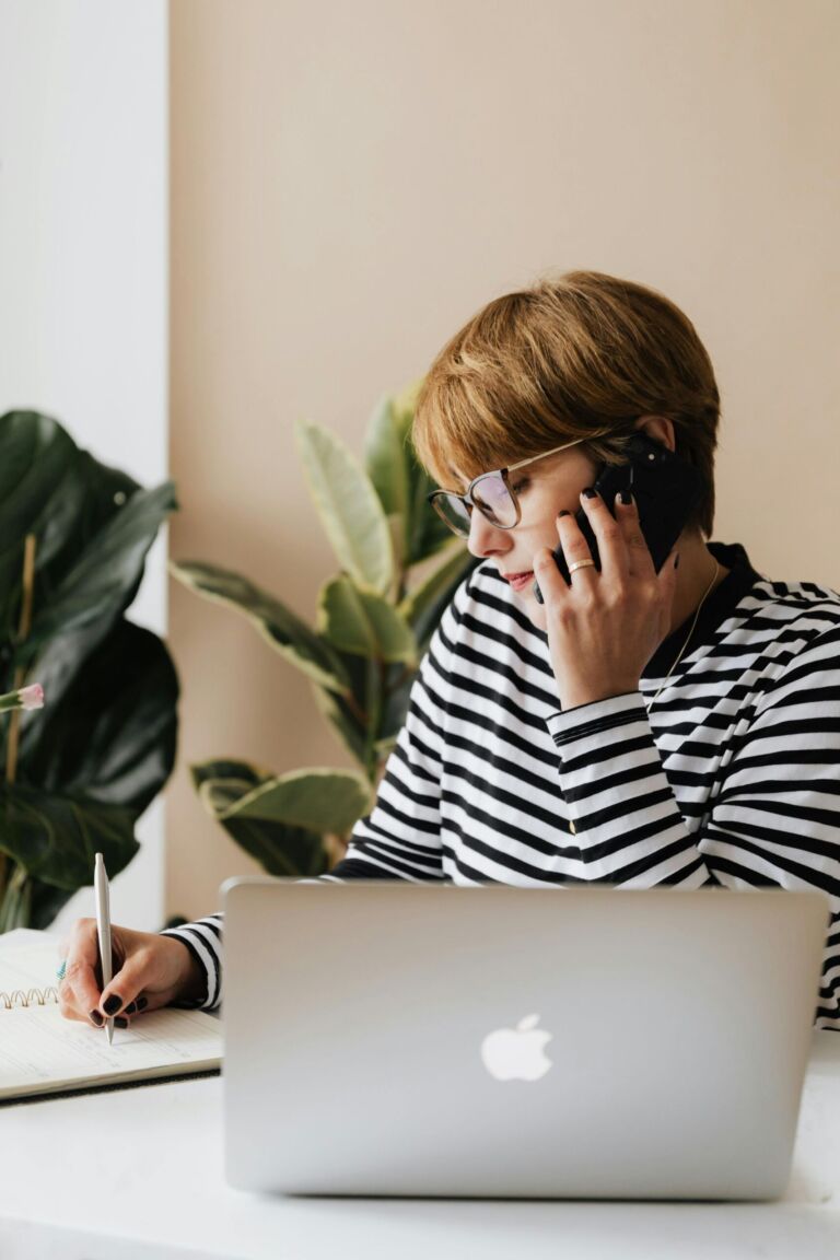 A person taking notes while on the phone at a desk