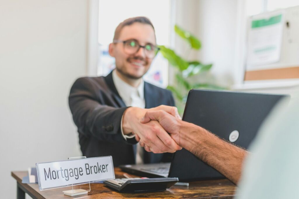 A mortgage broker shaking hands with a client at a desk