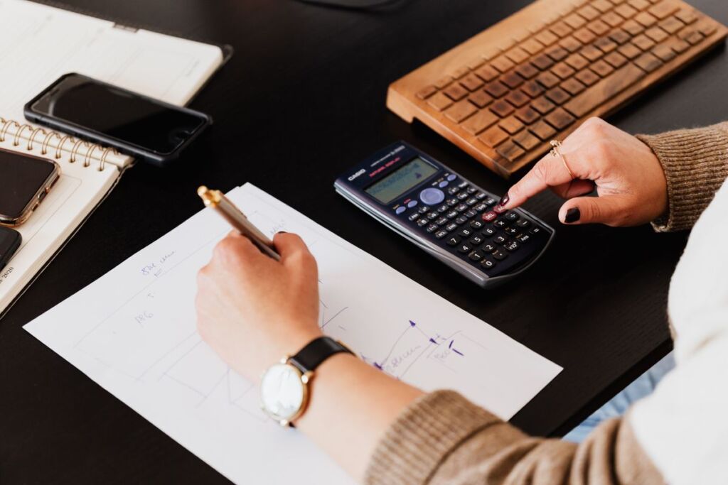Bookkeeper writing figures on paper while using a calculator